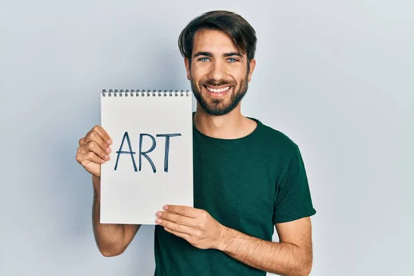 Joven Hombre Hispano Sosteniendo Cuaderno Arte Con Aspecto Positivo Feliz — Foto de Stock