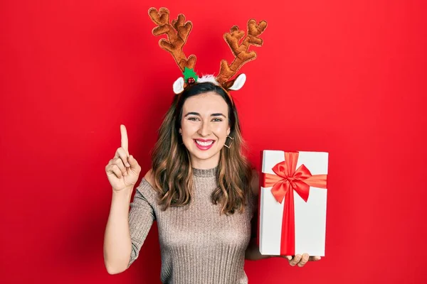 Joven Chica Hispana Con Sombrero Navidad Ciervo Sosteniendo Regalo Sonriendo —  Fotos de Stock