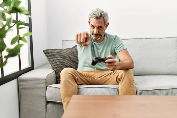 中年的他惊慌失措的男人坐在沙发上玩电子游戏 用手指着相机 对着你 自信地摆出一副严肃的姿势 — 图库照片