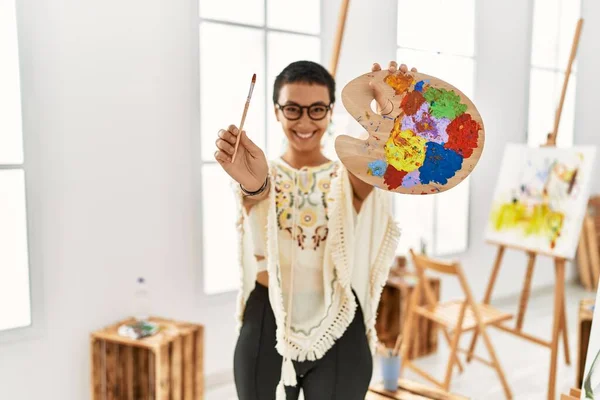 年轻的惊慌失措的女人微笑着 自信地拿着画笔和调色板在艺术工作室里 — 图库照片