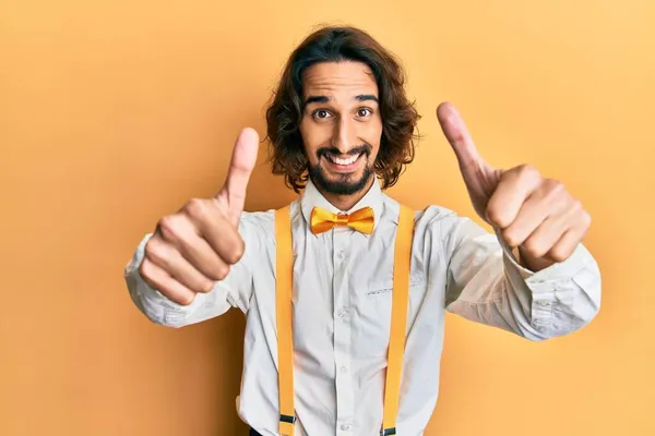 若いヒスパニック系の男性は 手で積極的なジェスチャーを行うことを承認ヒップスターエレガントな外観を身に着けている 親指アップ笑顔と成功のために幸せ 勝者のジェスチャー — ストック写真