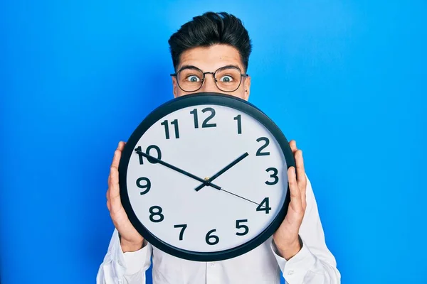 Joven Hombre Hispano Sosteniendo Gran Reloj Sobre Cara Celebrando Loco —  Fotos de Stock