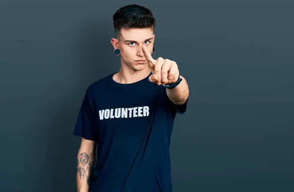 耳の拡張を身に着けている若い白人の少年ボランティアTシャツを指差して指を上げ 怒りの表情 ジェスチャーを示さない — ストック写真