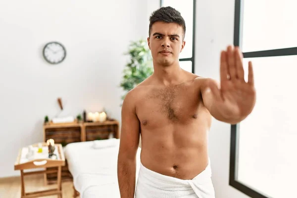 Young Hispanic Man Standing Shirtless Spa Center Doing Stop Sing — Zdjęcie stockowe