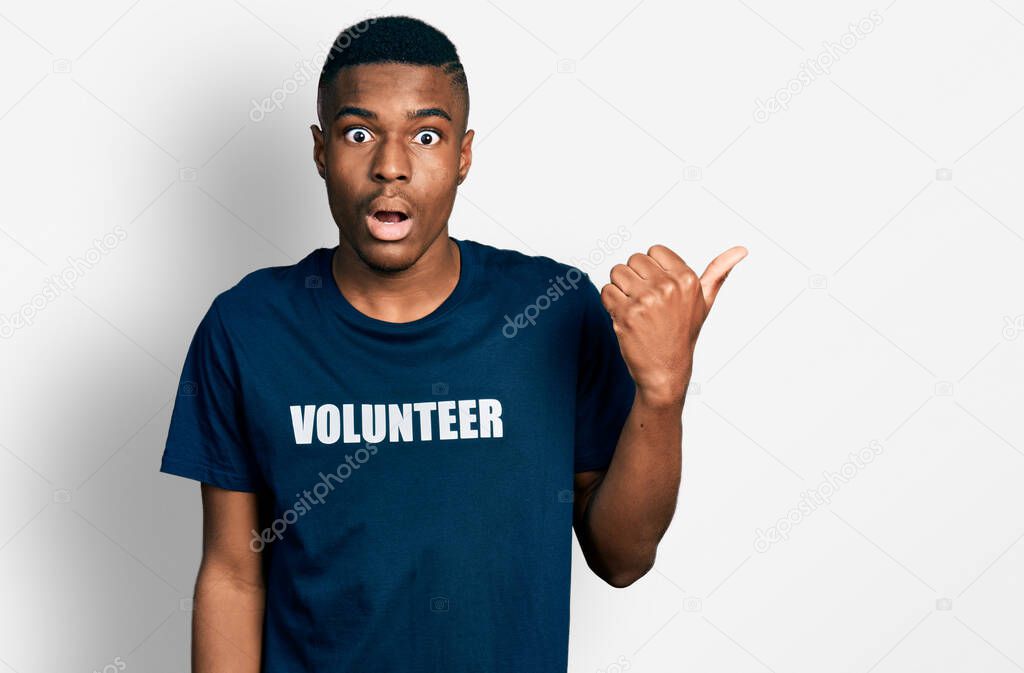 Young african american man wearing volunteer t shirt surprised pointing with hand finger to the side, open mouth amazed expression. 