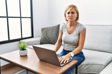 Orta yaşlı sarışın kadın evde dizüstü bilgisayar kullanıyor. Depresyonda ve endişe içinde. Kızgın ve korkmuş bir şekilde ağlıyor. hüzünlü ifade. 