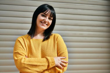 Genç esmer kadın mutlu gülümsüyor kolları çapraz kapılar ardında