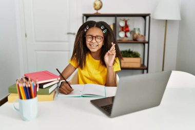 Young african american girl doing homework at home gesturing finger crossed smiling with hope and eyes closed. luck and superstitious concept. 
