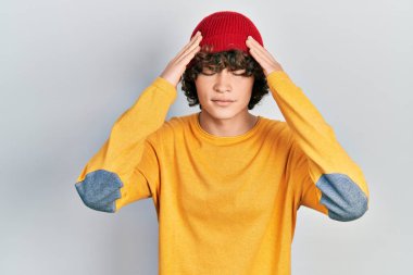 Handsome young man wearing wool hat with hand on head for pain in head because stress. suffering migraine. 