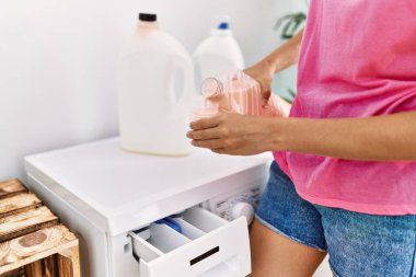 Çamaşır odasında çamaşır makinesi kullanan beyaz bir kadın.