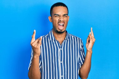 Sıradan kıyafetler giymiş, çılgın bir ifadeyle bağıran, elleri havada rock sembolü yapan genç bir Afrikalı Amerikalı. Müzik yıldızı. ağır kavram. 