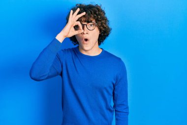 Handsome young man wearing casual clothes and glasses doing ok gesture shocked with surprised face, eye looking through fingers. unbelieving expression. 