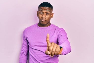 Genç siyah bir adam pembe bir süveter giyiyor. Parmağını kaldırmış ve kızgın bir ifade sergiliyor. 