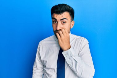 İş kıyafetleri giymiş genç İspanyol bir adam gergin ve elleri ağızda tırnak yerken gergin görünüyor. anksiyete. 