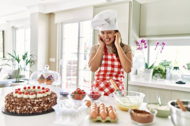 Güzel, genç, esmer pasta şefi kadın gürültülü müzik sesi için kulaklarını parmaklarıyla kapatarak pasta pişiriyor. sağır kavramı. 