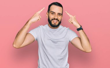 Sakallı, sıradan beyaz tişörtlü, iki eliyle başını gösteren genç adam. Harika fikir ya da düşünce, iyi hafıza. 