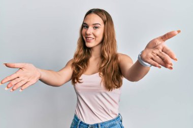 Kolsuz tişörtlü, gündelik tarzda giyinen genç sarışın kadın kucaklanmak için kollarını açmış kameraya bakıyor. Mutluluğu kucaklayan neşeli bir ifade.. 