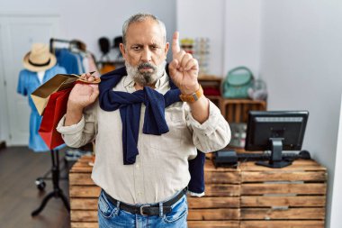 Butik dükkanında alışveriş torbaları tutan yakışıklı bir adam parmağını kaldırmış ve kızgın bir ifadeyle işaret ediyor, hiç hareket göstermiyor. 