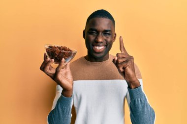 Genç Afro-Amerikalı elinde kuru üzümlü bir kaseyle gülümseyen bir adam bir numaralı mutlu yüzü işaret eden bir soru ya da fikirle 