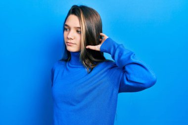 Boğazlı kazak giyen, boynu ağrıyan, eli boynuna dokunan, kas ağrısı çeken genç esmer kız. 