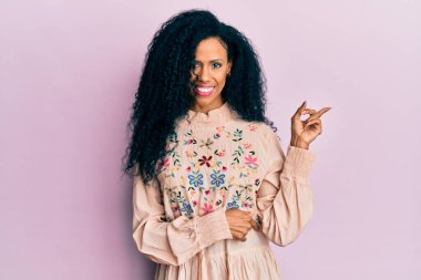 Orta yaşlı Afro-Amerikalı kadın, günlük kıyafetler giyip gülümsüyor. 