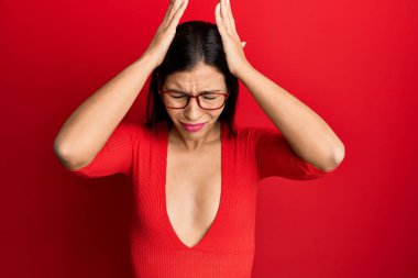 Genç Latin kadın gündelik kıyafetler ve gözlük takıyor. Baş ağrısı çekiyor, çaresiz ve stresli. Çünkü ağrı ve migren. Eller başının üstünde.. 