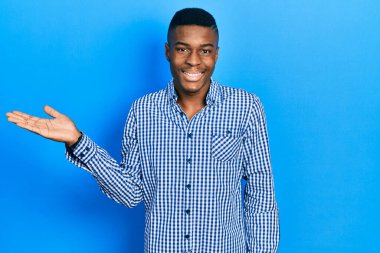 Genç Afrikalı Amerikalı sıradan kıyafetler giymiş neşeli bir şekilde gülümseyen ve avuç içi kameraya bakan biri.. 