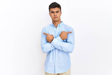 Young hispanic man wearing business shirt standing over isolated background pointing to both sides with fingers, different direction disagree 