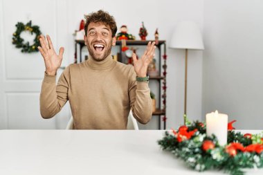 Noel süslemesi sırasında masanın üzerinde oturan sakallı yakışıklı genç adam çılgın ve başarıyı kollarını kaldırıp heyecanla haykırarak kutluyor. Kazanan konsept 