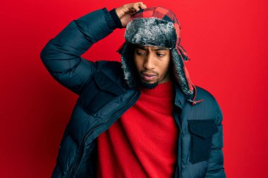 Sakallı, kışlık şapkası ve ceketi olan Afrikalı genç bir Amerikalı soru sorup şaşırıyor. Şüpheyle kararsız, kafa kafaya düşünerek. Düşünceli kavram. 