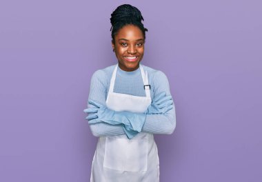 Önlük takan, kolları çapraz gülümseyen ve kameraya bakan Afro-Amerikan kadın. pozitif kişi. 