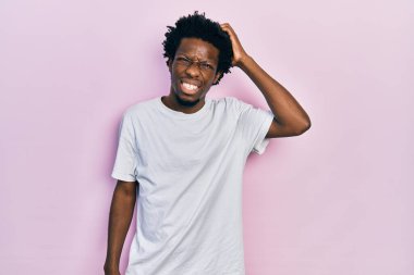 Gündelik beyaz t-shirt giyen genç Afro-Amerikan adam soru sorup kafasını karıştırıyor. Şüpheyle kararsız, kafa kafaya düşünerek. Düşünceli kavram. 