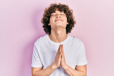 Handsome young man wearing casual white t shirt begging and praying with hands together with hope expression on face very emotional and worried. begging. 