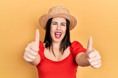 Yaz şapkası takan genç İspanyol kadın elleriyle olumlu jest yapmayı onaylıyor. Gülümsüyor ve başarı için seviniyor. kazanan jest. 