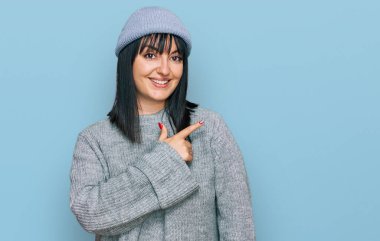 Şirin yün şapkalı, neşeli, yüzünde mutlu ve doğal bir ifadeyle elini ve parmağını gösteren bir gülümsemesi olan İspanyol genç bir kadın. 