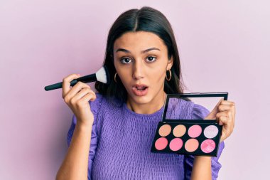 Makyaj fırçası tutan genç İspanyol kadın ve yüzü kızardı. Şüpheci ve alaycı görünüyordu. 