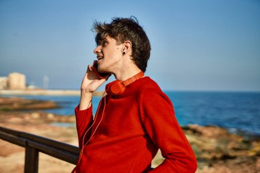 Genç İspanyol gülümseyen adam sahilde akıllı telefondan konuşarak mutlu oluyor.