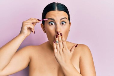 Güzel esmer kadın, kaşlarını fırçayla fırçalayıp ağızlarını eliyle kapatıyor, şok geçiriyor ve hata yapmaktan korkuyor. şaşırmış ifade 