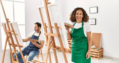 İspanyol orta yaşlı kadın ve sanat stüdyosunda olgun bir adam. Olumlu ve mutlu görünüyorlar. Kendine güvenen bir gülümsemeyle dişlerini gösteriyorlar. 