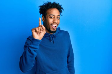 Sakallı, sıradan bir eşofman üstü giyen, bir fikir veya soruyla gülümseyen, mutlu bir yüzle işaret eden Afrikalı genç bir Amerikalı. 