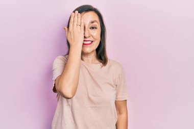 Orta yaşlı İspanyol kadın gündelik kıyafetler giyiyor. Bir gözünü eliyle kapatıyor. Yüzünde kendine güvenen bir gülümseme ve sürpriz bir duygu var.. 