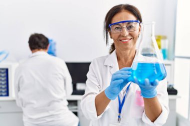 Laboratuvarda deney tüpü tutan bilim adamı üniforması giyen orta yaşlı erkek ve kadın partnerler.