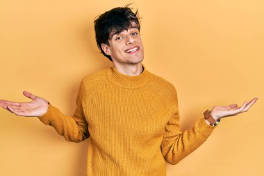 Yakışıklı hippi genç adam gündelik sarı süveter giyiyor gülümseyerek avuçlarını açıyor, sunuyor ve reklam karşılaştırması yapıyor ve dengeyi sağlıyor. 