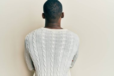 Gündelik giysiler giymiş genç Afro-Amerikan bir adam arkasını dönüp kollarını kavuşturarak başka tarafa bakıyor. 