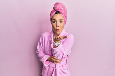 Duş başlığı ve bornoz takmış genç sarışın kadın kameraya bakıyor ve havada bir öpücük savuruyor. Güzel ve seksi. aşk ifadesi. 