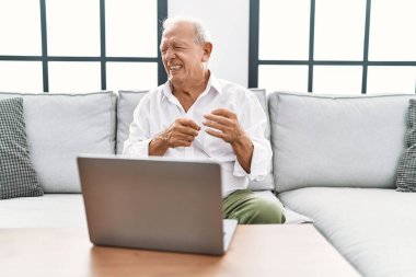 Evde dizüstü bilgisayar kullanan yaşlı bir adam iğrenç bir ifade takınıyor, tiksinti tepkisi yüzünden tiksinmiş ve korkmuş bir ifade takınıyor. Eller havada. 