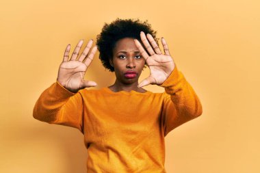 Genç Afro-Amerikalı kadın günlük kıyafetler giyip el ve parmaklarıyla çerçeve yapıyor, kamera bakış açısı var. 