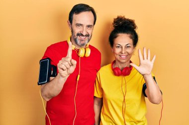 Orta yaşlı İspanyol kadın ve erkek spor giyer ve kol bandı takar. Altıncı parmaklarını gösterip gösterirken mutlu ve kendinden emin bir şekilde gülümserler.. 