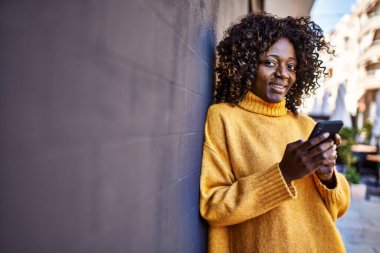 Afro-Amerikalı kadın sokakta akıllı telefon kullanarak kendine güveniyor.