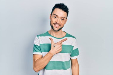 Gündelik kıyafetler giyen, neşeli, yüzünde gülümseme olan genç İspanyol adam mutlu ve doğal bir ifadeyle elini ve parmağını kaldırdı. 